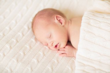 Beyaz güneşli yatak odasında sevimli bir bebek. Yeni doğmuş çocuk yatakta dinleniyor. Küçük çocuklar için çocuk odası. Çocuklar için tekstil ve yatak. Aile sabahı evde. Oyuncak ayıyla karnını doyururken doğan yeni çocuk..