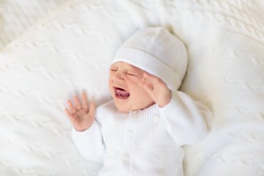 Beyaz güneşli yatak odasında sevimli bir bebek. Yeni doğmuş çocuk yatakta dinleniyor. Küçük çocuklar için çocuk odası. Çocuklar için tekstil ve yatak. Aile sabahı evde. Oyuncak ayıyla karnını doyururken doğan yeni çocuk..