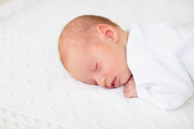 Beyaz güneşli yatak odasında sevimli bir bebek. Yeni doğmuş çocuk yatakta dinleniyor. Küçük çocuklar için çocuk odası. Çocuklar için tekstil ve yatak. Aile sabahı evde. Oyuncak ayıyla karnını doyururken doğan yeni çocuk..