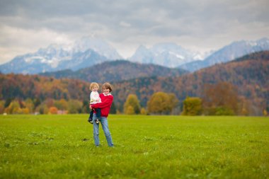 Dağlarda yürüyüş yapan çocuklu bir aile. Genç anne ve çocuklar güzel Alpler dağ manzarasında yürüyüş yapıyorlar. Bebekle seyahat et. Küçük bir çocukla gezmek ve kamp yapmak. Açık hava macerası.