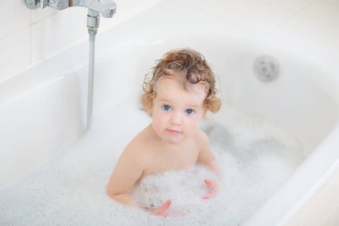 Küvette sabun köpüğüyle oynayan küçük bir bebek. Küçük kız dişlerini fırçalıyor ve saçlarını şampuanla yıkıyor. Bebek için duş yıkama. Anne banyo bebeği..