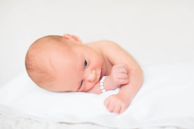 Beyaz güneşli yatak odasında sevimli bir bebek. Yeni doğmuş çocuk yatakta dinleniyor. Küçük çocuklar için çocuk odası. Çocuklar için tekstil ve yatak. Aile sabahı evde. Oyuncak ayıyla karnını doyururken doğan yeni çocuk..
