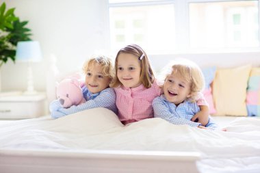 Çocuklar yatakta oynar. Çocuklar beyaz güneşli yatak odasında. Kardeş pijamalarıyla ebeveyn odasında oynuyorlar. Aile sabahı. Oğlan ve kız uyanın ya da uyuyun..