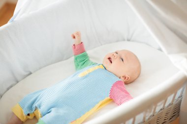 Beyaz güneşli yatak odasında beşikteki sevimli bebek. Yeni doğmuş çocuk yatakta dinleniyor. Küçük çocuklar için çocuk odası. Çocuklar için tekstil ve yatak. Aile sabahı evde. Oyuncak ayıyla karnını doyururken doğan yeni çocuk..