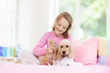 Bebek köpek ve kediyle oynayan çocuk. Çocuklar köpek yavrusu ve kedi yavrusu ile oynarlar. Küçük kız ve Amerikan cocker spaniel evde yatakta. Çocuklar ve evcil hayvanlar evde. Çocuk evcil hayvanla şekerleme yapıyor. Hayvan bakımı.