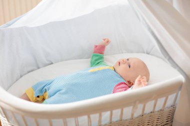 Beyaz güneşli yatak odasında beşikteki sevimli bebek. Yeni doğmuş çocuk yatakta dinleniyor. Küçük çocuklar için çocuk odası. Çocuklar için tekstil ve yatak. Aile sabahı evde. Oyuncak ayıyla karnını doyururken doğan yeni çocuk..