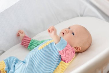 Yeni doğan bebek çocuk yatakta bir güneşli sabah oynarken. Yeni doğan çocuk beşik içinde rahatlatıcı. Çocuk uyku. Yatak takımları ve çocuklar için giysi. Bebek yatakta uyuyor. Sağlıklı çocuk doğumdan kısa bir süre sonra. 