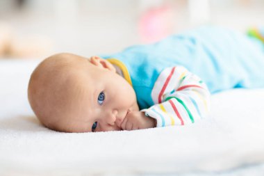 Beyaz güneşli yatak odasında sevimli bir bebek. Yeni doğmuş çocuk yatakta dinleniyor. Küçük çocuklar için çocuk odası. Çocuklar için tekstil ve yatak. Aile sabahı evde. Gökkuşağı battaniyeli yeni doğmuş çocuk.