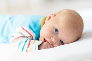 Beyaz güneşli yatak odasında sevimli bir bebek. Yeni doğmuş çocuk yatakta dinleniyor. Küçük çocuklar için çocuk odası. Çocuklar için tekstil ve yatak. Aile sabahı evde. Gökkuşağı battaniyeli yeni doğmuş çocuk.