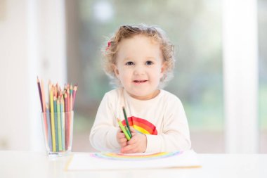 Çocuklar resim yapar. Beyaz güneşli çalışma odasında çocuk resimleri. Gökkuşağı çizen küçük kız. Okul çocuğu resim ödevi yapıyor. Çocuklar için sanat ve el sanatları. Çocuk ellerinde boya. Yaratıcı küçük sanatçı iş başında.