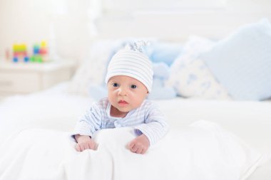 Beyaz güneşli yatak odasında sevimli bir bebek. Yeni doğmuş çocuk yatakta dinleniyor. Küçük çocuklar için çocuk odası. Çocuklar için tekstil ve yatak. Aile sabahı evde. Oyuncak ayıyla karnını doyururken doğan yeni çocuk..