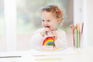 Çocuklar resim yapar. Beyaz güneşli çalışma odasında çocuk resimleri. Gökkuşağı çizen küçük kız. Okul çocuğu resim ödevi yapıyor. Çocuklar için sanat ve el sanatları. Çocuk ellerinde boya. Yaratıcı küçük sanatçı iş başında.