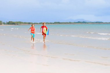 Tropik plajda oynayan çocuklar. Çocuklar yaz tatilinde yüzer ve denizde oynarlar. Kum ve su eğlencesi, küçük çocuklar için güneş koruması. Okyanus kıyısında koşan ve zıplayan küçük çocuk.