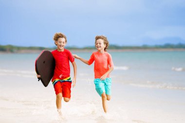 Tropik plajda oynayan çocuklar. Çocuklar yaz tatilinde yüzer ve denizde oynarlar. Kum ve su eğlencesi, küçük çocuklar için güneş koruması. Okyanus kıyısında koşan ve zıplayan küçük çocuk.