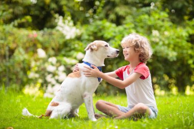 Güneşli yaz bahçesinde bir köpekle oynayan çocuk. Çocuk yürüyen köpek yavrusu. Çocuklar ve evcil hayvanlar. Hayvani sevgi ve bağlılık. Evcil hayvanlı çocuk. En iyi arkadaşlar. Çocuklar ve hayvanlar dostluk.