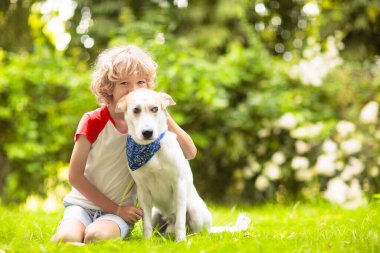 Güneşli yaz bahçesinde bir köpekle oynayan çocuk. Çocuk yürüyen köpek yavrusu. Çocuklar ve evcil hayvanlar. Hayvani sevgi ve bağlılık. Evcil hayvanlı çocuk. En iyi arkadaşlar. Çocuklar ve hayvanlar dostluk.