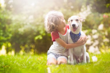 Güneşli yaz bahçesinde bir köpekle oynayan çocuk. Çocuk yürüyen köpek yavrusu. Çocuklar ve evcil hayvanlar. Hayvani sevgi ve bağlılık. Evcil hayvanlı çocuk. En iyi arkadaşlar. Çocuklar ve hayvanlar dostluk.