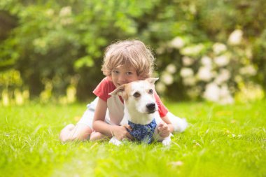 Güneşli yaz bahçesinde bir köpekle oynayan çocuk. Çocuk yürüyen köpek yavrusu. Çocuklar ve evcil hayvanlar. Hayvani sevgi ve bağlılık. Evcil hayvanlı çocuk. En iyi arkadaşlar. Çocuklar ve hayvanlar dostluk.