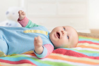 Beyaz güneşli yatak odasında, renkli gökkuşağı battaniyesinde sevimli bir bebek. Yeni doğmuş çocuk yatakta dinleniyor. Küçük çocuklar için çocuk odası. Çocuklar için tekstil ve yatak. Aile sabahı evde.. 