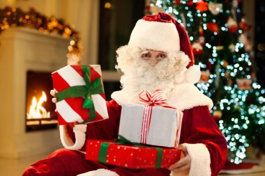 Noel Baba Noel arifesinde hediye getiriyor. Xmas ağacının altında hediyeler. Şömine ve ışıklarla dekore edilmiş oturma odası. Evde kış tatili kutlaması.