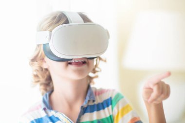 Sanal gerçeklik gözlüklü çocuk. Çocuklar için video kayıt seti. Küçük çocuk bilgisayar oyunu oynuyor. Modern dijital cihazla öğreniyorum. Çocuklar elektronik aletlerle ders çalışırlar. Gelecek eğitim konsepti. Eğlenceli oyun..