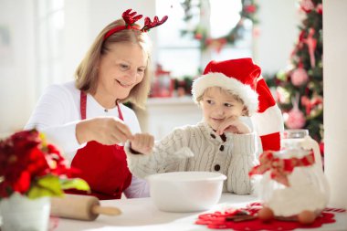 Aile Noel kurabiyesi pişiriyor. Büyükanne ve çocuk zencefilli kek pişirir. Çocuklar Xmas eğlencesi. Noel Baba şapkalı küçük çocuk kış kurabiyesi için hamur yapıyor. Ev tatili dekorasyonu.