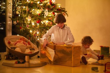 Evde Noel ağacı süsleyen çocuk. Xmas süslemeli pijamalı küçük bir kız ve oğlan. Çocuklu aile kış tatilini kutlar. Çocuklar Noel için oturma odasını ve şömineyi dekore ederler..