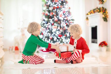 Noel arifesinde Noel ağacı ve şömine başında çocuklar. Noel 'i evde kutlayan çocuklu bir aile. Erkek ve kız aynı pijamaları giyip Noel ağacını süslüyor ve hediyeleri açıyor. Çocuklar için tatil hediyeleri.