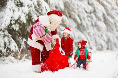 Karlı ormanda Noel hediyeli çocuklar ve Noel Baba. Çocuklar kar parkında Noel Baba 'ya yardım ediyor. Eğlenceli kızak gezisi. Noel tatili eğlencesi. Noel Baba hediyeler ve elflerle. Kış tatili.