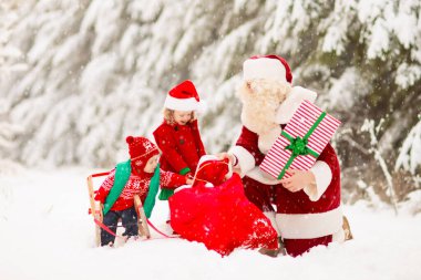 Karlı ormanda Noel hediyeli çocuklar ve Noel Baba. Çocuklar kar parkında Noel Baba 'ya yardım ediyor. Eğlenceli kızak gezisi. Noel tatili eğlencesi. Noel Baba hediyeler ve elflerle. Kış tatili.