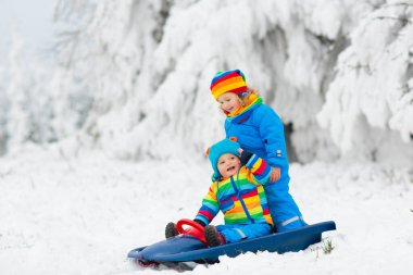 Çocuklar kış parkında karda oynarlar. Çocuklar karlı soğuk bir günde dışarıda oynuyorlar. Oğlan ve kız kızakla gezerken eğleniyorlar. Noel tatili aktivitesi. Kış havasında açık hava eğlencesi. Çocukla seyahat et..