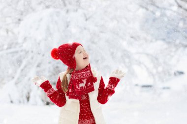 Kırmızı şapkalı çocuk Noel tatilinde karda oynuyor. Kış açık hava eğlencesi. Çocuklar Noel arifesinde karlı parkta oynarlar. Örgü süveter, atkı ve Noel süslemeli eldivenli küçük kız..