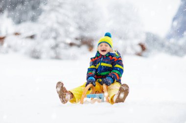 Küçük çocuk kızakla gezintiye çıkıyor. Çocuk kayağı. Kızak süren küçük bir çocuk. Çocuklar karda dışarıda oynarlar. Çocuklar kışın Alp dağlarında kızak kullanırdı. Aile Noel tatili için açık hava eğlencesi.