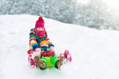 Çocuklar kış parkında karda oynarlar. Çocuklar karlı soğuk bir günde dışarıda oynuyorlar. Oğlan ve kız kızakla gezerken eğleniyorlar. Noel tatili aktivitesi. Kış havasında açık hava eğlencesi. Çocukla seyahat et..