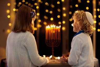 Çocuklar Hanuka 'yı kutluyor. Yahudi ışık festivali. Çocuklar geleneksel menoranın üzerinde mum yakıyor. Kippah 'ta Dreidel ve Sufganiyah çörekli bir çocuk. İsrail tatili.