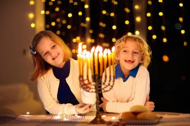 Çocuklar Hanuka 'yı kutluyor. Yahudi ışık festivali. Çocuklar geleneksel menoranın üzerinde mum yakıyor. Kippah 'ta Dreidel ve Sufganiyah çörekli bir çocuk. İsrail tatili.
