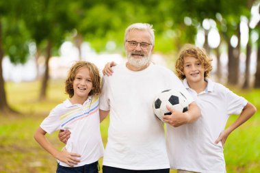 Büyükbaba ve çocuklar güneşli parkta futbol oynuyorlar. Mutlu aile top oynuyor. Büyükbaba ve çocuklar futbol oynarlar. Nesil aşkı. Aktif kıdemli adam ve küçük çocuk. Torunlar dedeleri ziyaret ediyor..