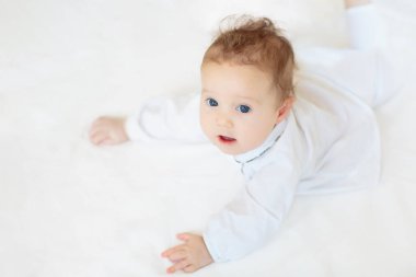Beyaz güneşli yatak odasında sevimli bir bebek. Yeni doğmuş çocuk yatakta dinleniyor. Küçük çocuklar için çocuk odası. Çocuklar için tekstil ve yatak. Aile sabahı evde. Örgü kazaklı çocuk..