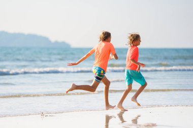 Tropik plajda oynayan çocuklar. Çocuklar yaz tatilinde yüzer ve denizde oynarlar. Kum ve su eğlencesi, küçük çocuklar için güneş koruması. Okyanus kıyısında koşan ve zıplayan küçük çocuk.