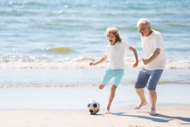 Büyükbaba ve çocuklar yaz plajında futbol oynarlar. Aile günü dışarıda. Büyükbaba ve torunlar futbol oynuyor. Nesil aşkı. Torunumla top oynayan kıdemli aktif bir adam. Mutlu emeklilik.