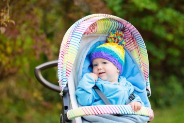 Bebek arabasındaki bebek sonbahar parkta bir yürüyüş. Örgü şapka ve ceket sıcak battaniye altında renkli olayından oturan sevimli küçük çocuk. Sonbahar açık eğlenceli çocuklar için. Çocuk arabası kışın içinde yürüyüş.