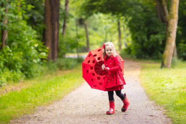 Küçük kız yağmurlu yaz parkta oynarken. Çocuk ile kırmızı uğur böceği şemsiye, ceket ve su birikintisine atlama bot su geçirmez ve yağmurda çamur. Sonbahar duş yürüyüş çocuk. Herhangi bir hava açık eğlence.