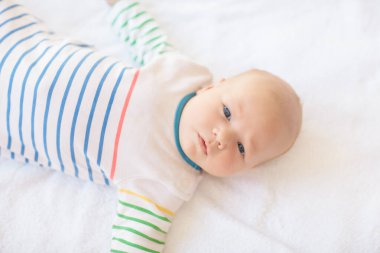 Beyaz güneşli yatak odasında sevimli bir bebek. Yeni doğmuş çocuk yatakta dinleniyor. Küçük çocuklar için çocuk odası. Çocuklar için tekstil ve yatak. Aile sabahı evde. Oyuncak ayıyla karnını doyururken doğan yeni çocuk..