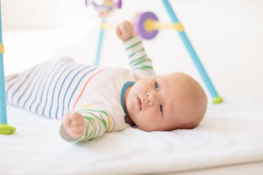 Beyaz güneşli yatak odasında sevimli bir bebek. Yeni doğmuş çocuk yatakta dinleniyor. Küçük çocuklar için çocuk odası. Çocuklar için tekstil ve yatak. Aile sabahı evde. Oyuncak ayıyla karnını doyururken doğan yeni çocuk..