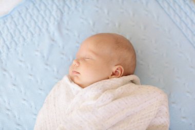 Beyaz güneşli yatak odasında sevimli bir bebek. Yeni doğmuş çocuk yatakta dinleniyor. Küçük çocuklar için çocuk odası. Çocuklar için tekstil ve yatak. Aile sabahı evde. Oyuncak ayıyla karnını doyururken doğan yeni çocuk..