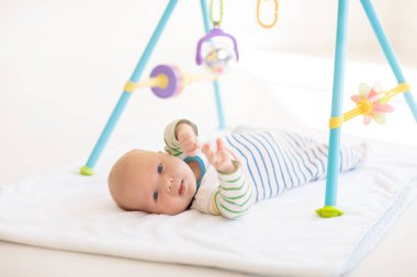 Beyaz güneşli yatak odasında sevimli bir bebek. Yeni doğmuş çocuk yatakta dinleniyor. Küçük çocuklar için çocuk odası. Çocuklar için tekstil ve yatak. Aile sabahı evde. Oyuncak ayıyla karnını doyururken doğan yeni çocuk..