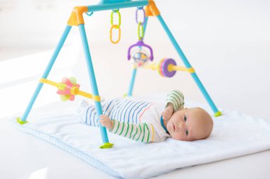 Beyaz güneşli yatak odasında sevimli bir bebek. Yeni doğmuş çocuk yatakta dinleniyor. Küçük çocuklar için çocuk odası. Çocuklar için tekstil ve yatak. Aile sabahı evde. Oyuncak ayıyla karnını doyururken doğan yeni çocuk..