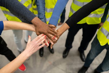 Yansıtıcı yelek giyen ve ellerini birleştirip birlik gösteren çok ırklı işçi grubunu kapatın. Takım çalışması konsepti.