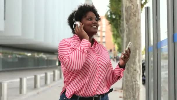 一个年轻的非洲裔美国人加上尺寸较大的女人用耳机听智能手机里的音乐的肖像 — 图库视频影像