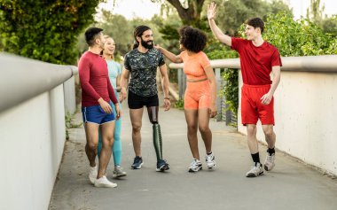 Çok ırklı bir grup atletik arkadaş dışarıda egzersiz yaparken protez bacakla arkadaşlarını destekliyor.